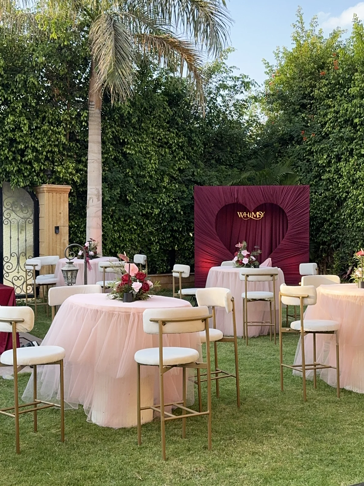 Pink-draped tables, floral arrangements and WHIMSY’s burgundy heart backdrop in the garden